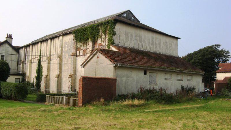 A large building, with moss running down the sides, surrounded by grass