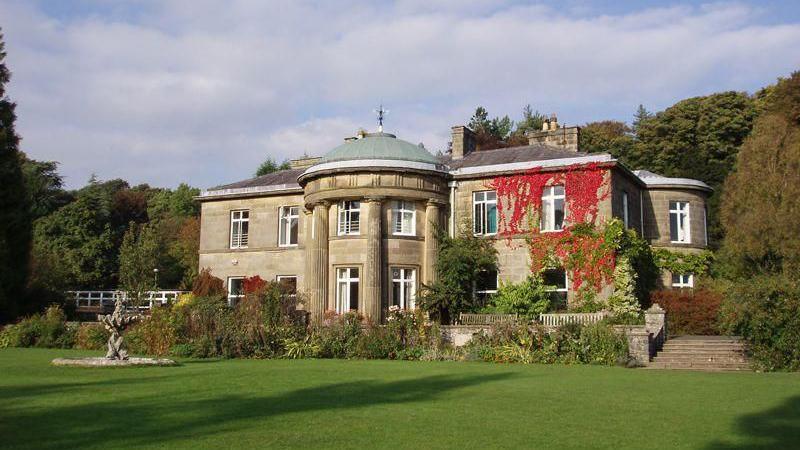 A large house with pillars at the front entrance sitting in manicured gardens