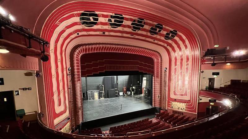 The New Theatre stage, which is surrounded by a large red facade. there are rows of red seats in front of it.