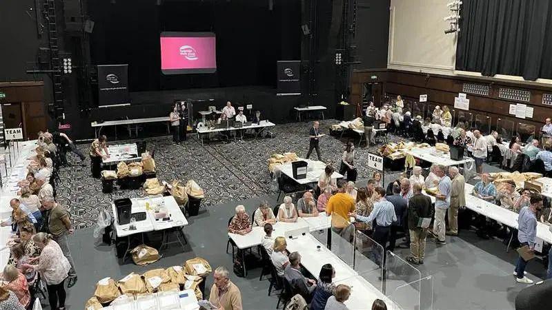A room filled with people on white tables at an election count in Kent