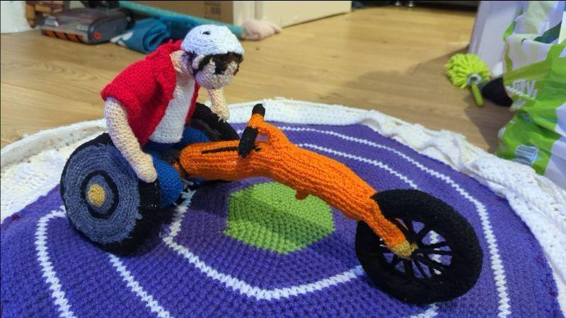 A knitted character riding a bike, propelled by the rider's hands