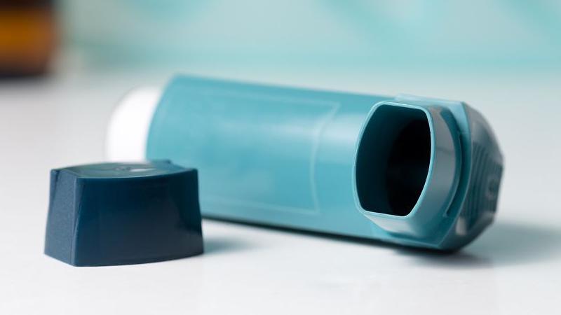 A light blue inhaler, with a dark blue lid laid on its side on a white table. 