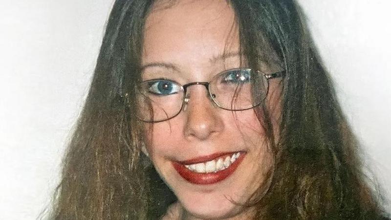 A woman with brown hair wearing glasses and smiling into the camera.