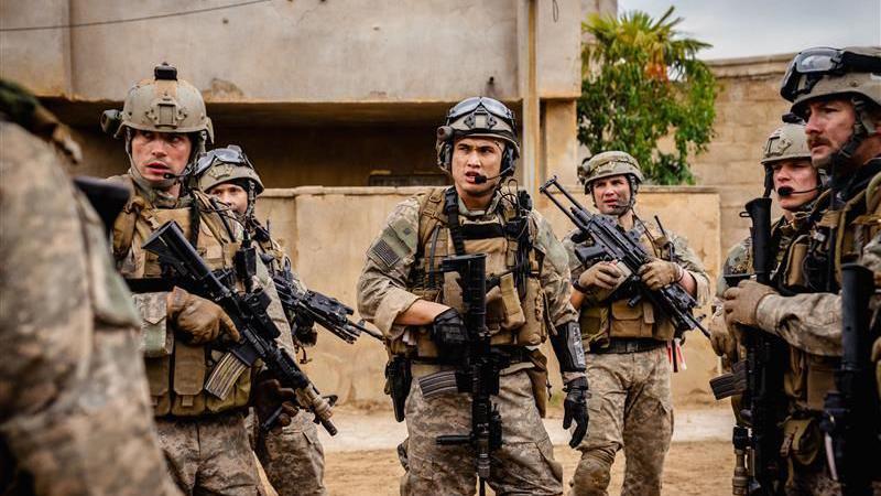 A screenshot of the movie, showing Aaron Mackenzie and other actors in military uniforms holding guns.