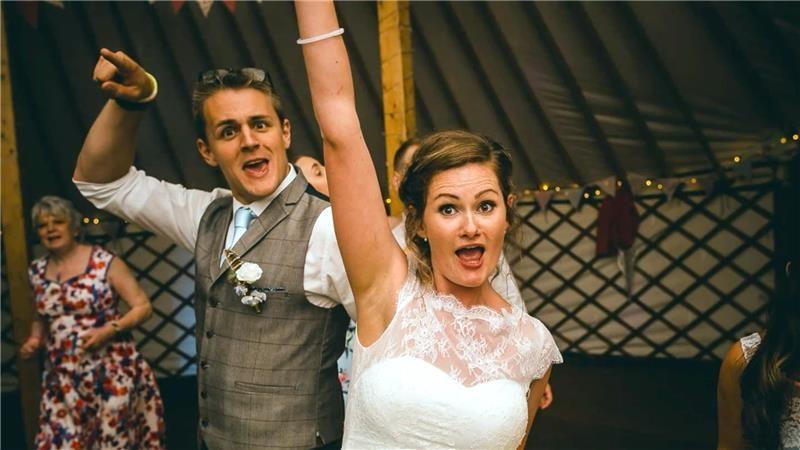 Henry and Rebecca on their wedding day. they are dancing and each have an arm in the air. they are inside a large marquee.