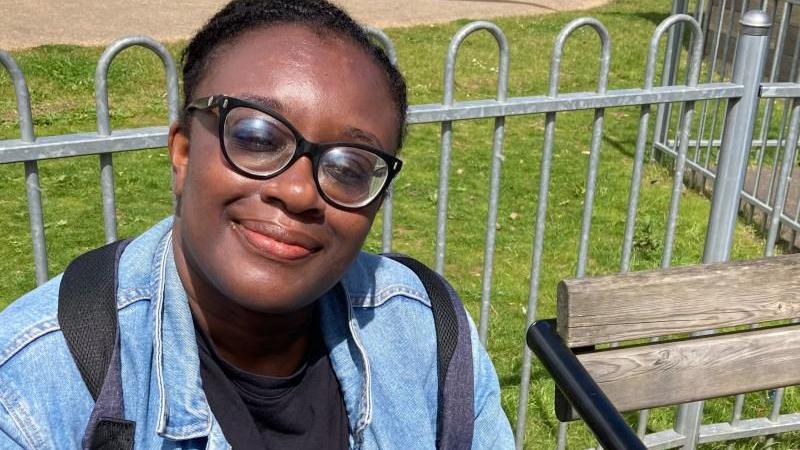 Catherine Yeboah in blue jacket sitting on park seat