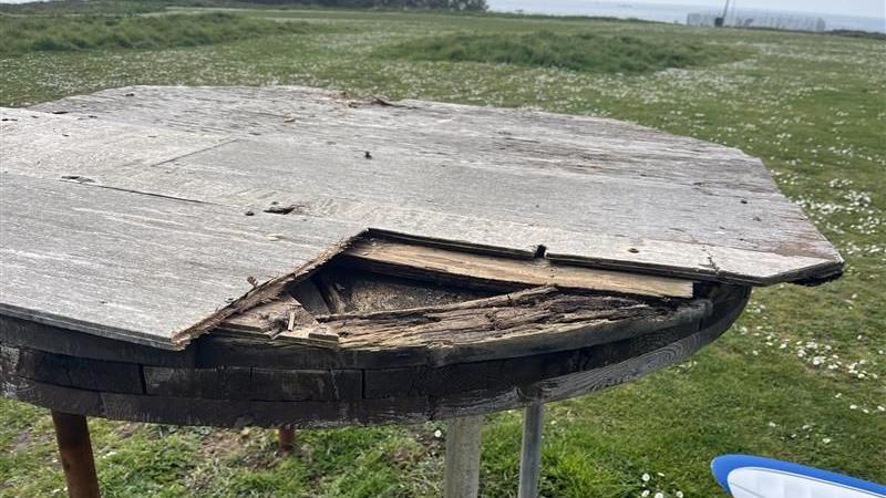 The corner of a damaged wooden table on a grassy area.