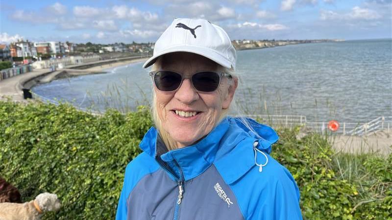 Close up image of June Wright wearing sunglasses and a cap overlooking West Bay at Westgate