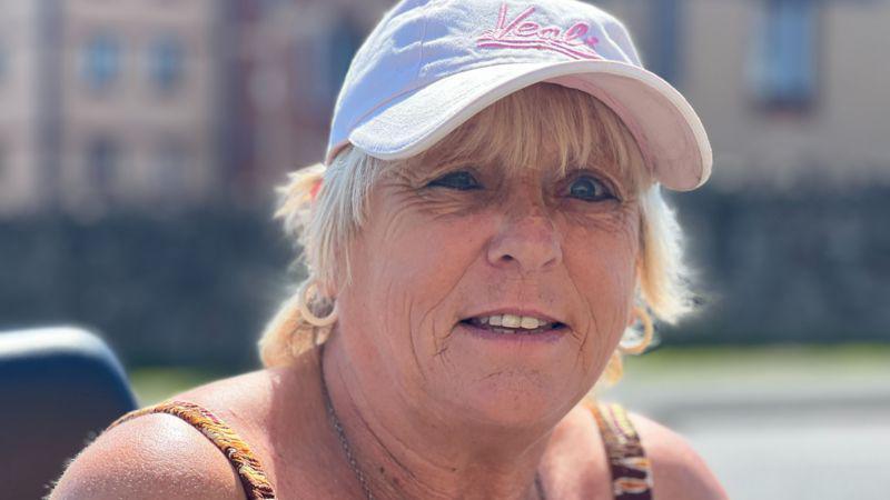 Jacqueline Smith. She has short blonde hair and blue eyes. She is wearing a white cap with pink writing on the front. She is pictured looking at the camera and smiling slightly. 