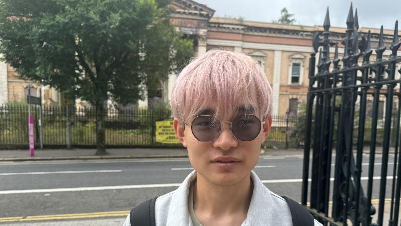 Xiao has short, light-pink hair and is wearing sunglasses and a grey jacket 