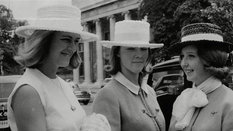 (L-R) Queen Camilla, then Camilla Shand, stands outdoors in a hat and pale dress, beside Virginia Crookshank and Rosemary Boord, both in hats and jackets, at Lords Cricket Ground. All three women are smiling