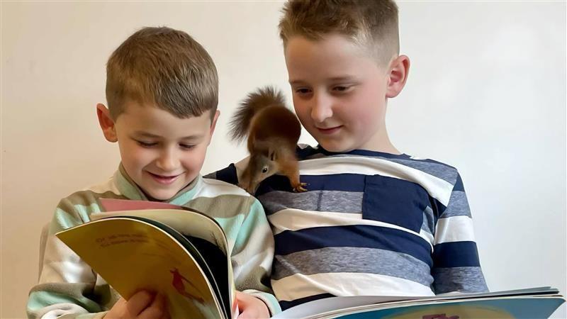 Brothers Pheonix and Morgan read with a red squirrel on Morgan's shoulder.