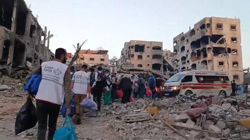 Screenshot from a video shows people evacuating, some wearing vests with the hospital's name on the back, carrying bags toward ambulances