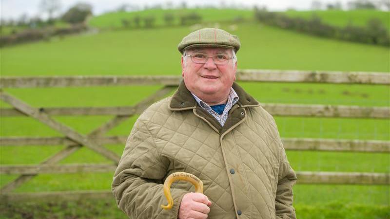 Dai Jones yn gwisgo cap fflat a siaced werdd caci a sbectol.