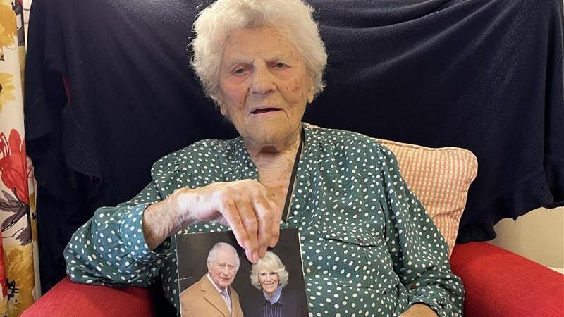 Ethel Caterham sat holding a card with a picture of the King and Queen on the cover.