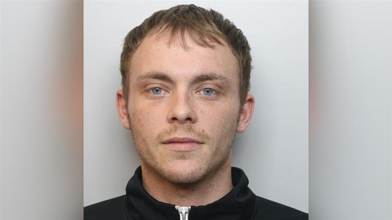 A man in a black zip up hoodie looks at the camera for his police mug shot.