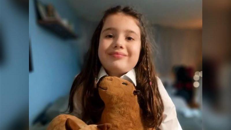 A girl with long brown hair cuddles a stuffed toy capybara