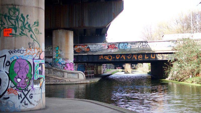 The huge concrete supports under Spaghetti Junction. A canal flows underneath it and there is some graffiti on the pillars. 