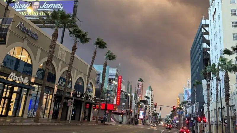 Dark skies and smoke rising above a largely empty commercial street lined with shops