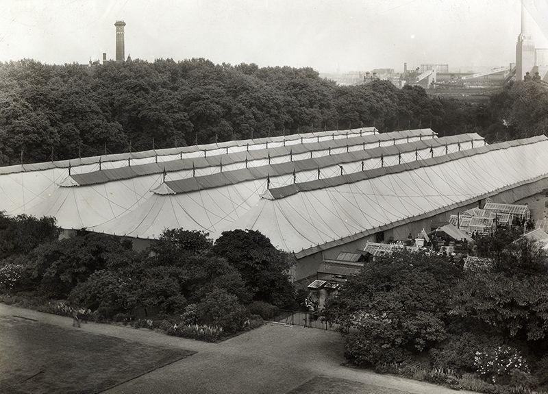 A black and white photo of a large marquee with four lines of pitched roofs.