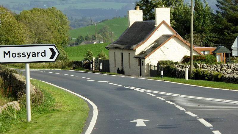 The A75 road through Dumfries and Galloway with a small white house at the roadside and rolling hills in the background