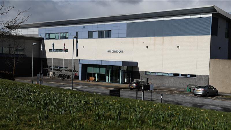 A view of the entrance at HMP Glenochil - the building is blue, white and grey and has two cars parked outside. There is a stretch of grass in the foreground.