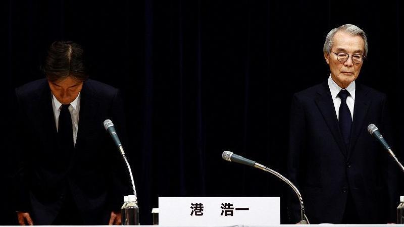 Fuji TV president Koichi Minato and chairman Shuji Kano standing in front of microphones at a press conference. Minato is bowing.