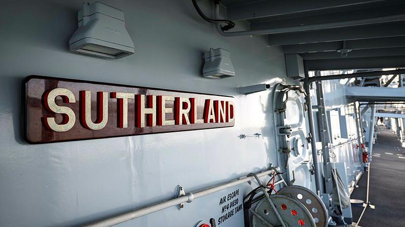 Onboard HMS Sutherland. There is a red sign on the left-hand side with the ship's name and a reel at the bottom. 