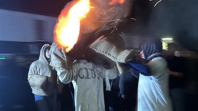 A flaming tar barrel on the back of a man with several other people gathered around.