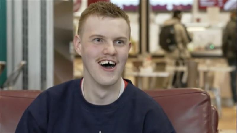 Christian Wilson sitting down on brown sofa, smiling