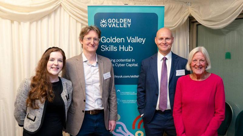 A group of four people, all dressed smartly, stand in front of a "Golden Valley Skills Hub" banner at an event at the House of Commons. There are cream-coloured curtains draped behind them. The people are a young woman with long, ginger hair, a young man with glasses and mid-length blond hair, a bald man, and an older woman with a light-coloured bob. All of them are smiling.