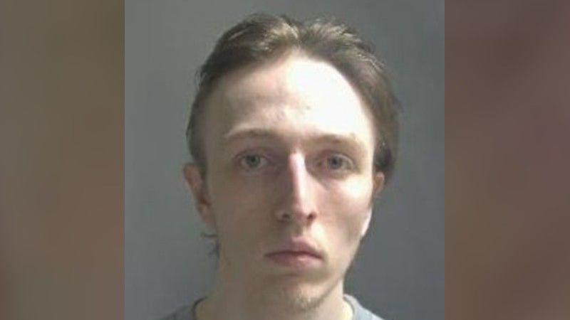 Jacob Clark looks directly at the camera as he is photographed in custody. He has brown hair scraped back off his face.