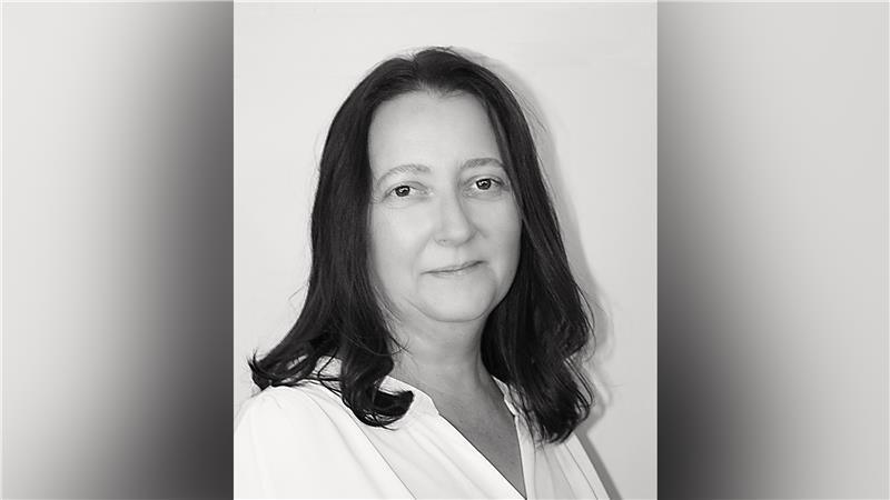 A black and white image of a woman with shoulder length brown hair and a white top.