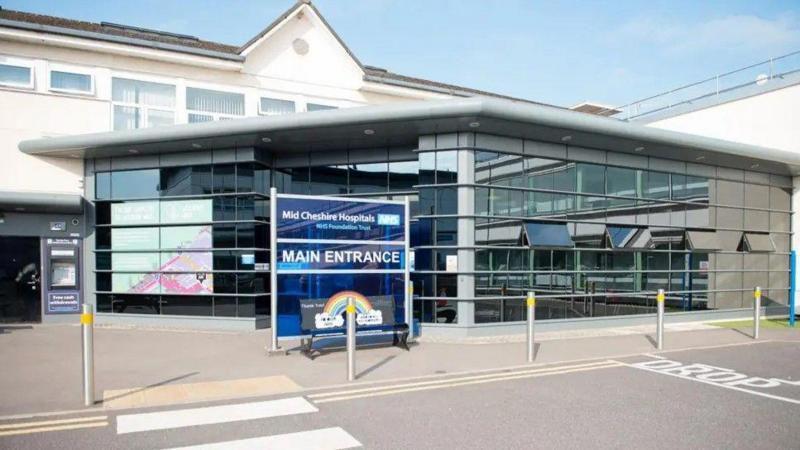 The front of Leighton Hospital, a modern glass entrance to an older building. There is a blue sign that says "main entrance".