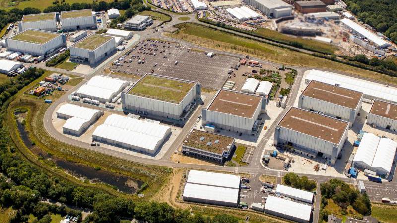 An aerial view of Pinewood Studios showing a number of film sets, car parks, roofs, buildings and foliage. 