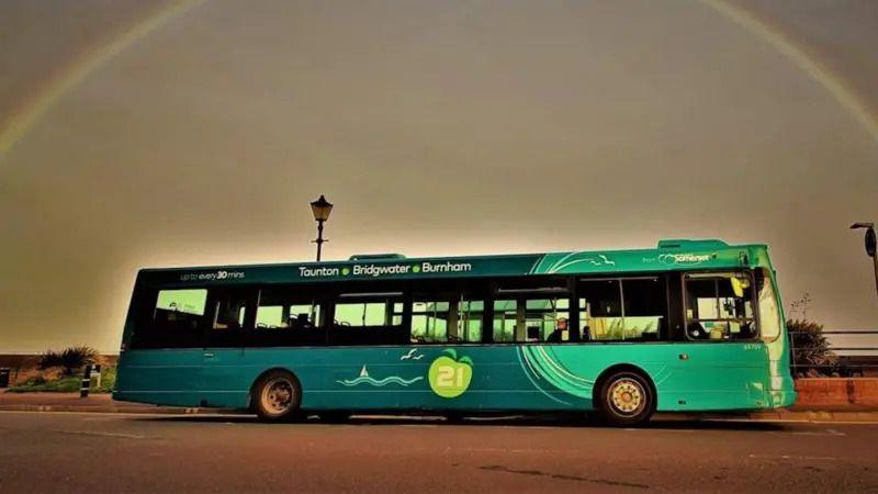 A green single decker bus against a darkening sky