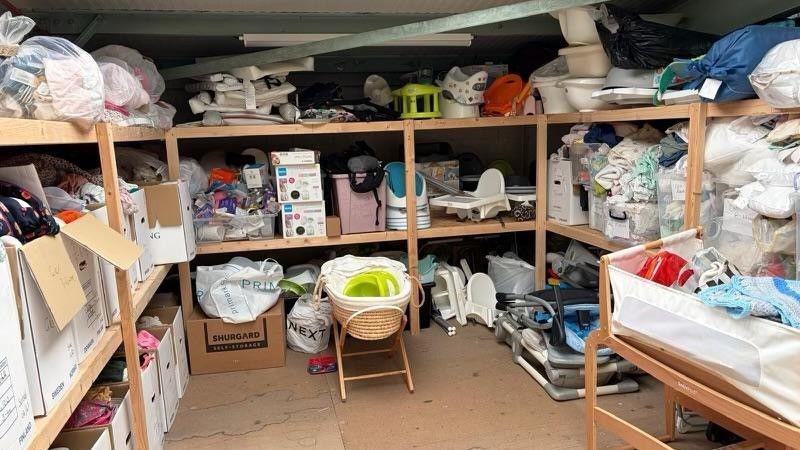 A storeroom with lots of donated baby items in it, including Moses baskets, chairs, cots, bags and boxes. 