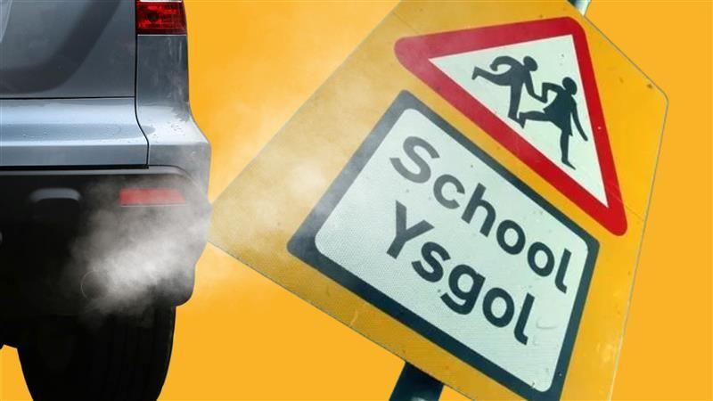 A car exhaust with fumes and a Welsh school sign.