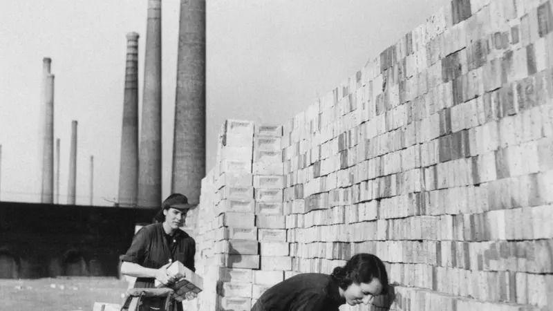 Black and white image of two people working at Stewartby in 1942. Chimneys are visible behind them