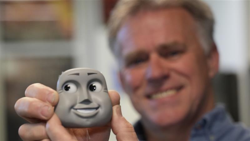 Sculptor Sean Hedges-Quinn holds a sculpted face from Thomas & Friends series. He can be seen slightly blurred in the background.