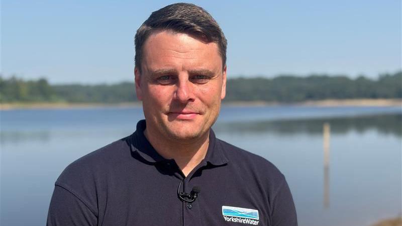Andy Shaw, head of water production at Yorkshire Water, wearing a blue branded polo shirt with a body of water in the background.