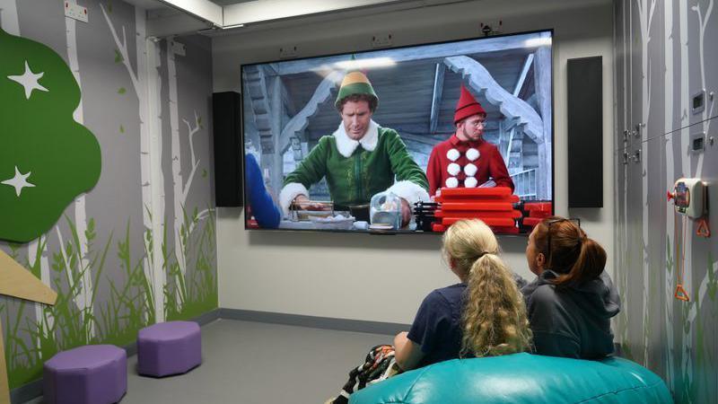 Two young girls sitting on a turquoise beanbag looking at home cinema screen with a scene from the film Elf on it