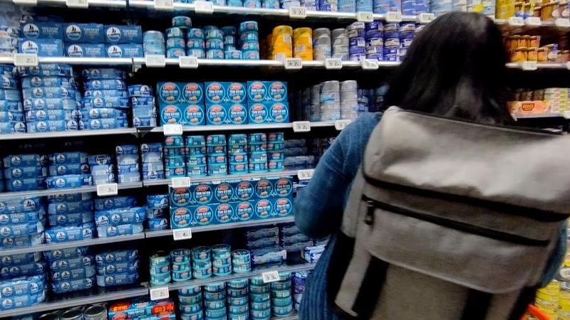 Tinned tuna sits on a shop shelf as a customer looks at it