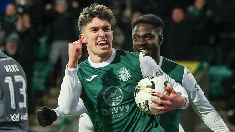 Hibs striker Kieron Bowie celebrates as he clenches his right fist and carries the ball in his left hand