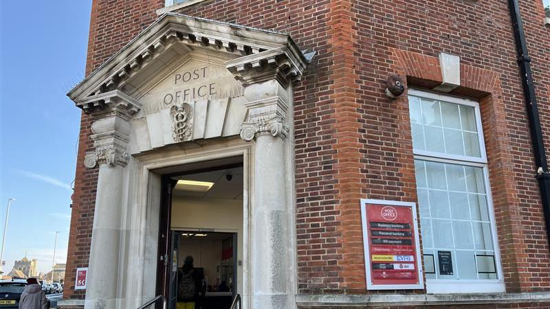 The red bricked Bexhill Post Office has large windows and is three storey's tall. It has two large stone pillars on either side of the main entrance and is engraved with the words post office on it