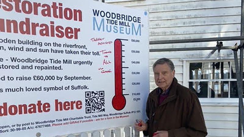 A man standing next to a sign showing that the target for restoration work was met 