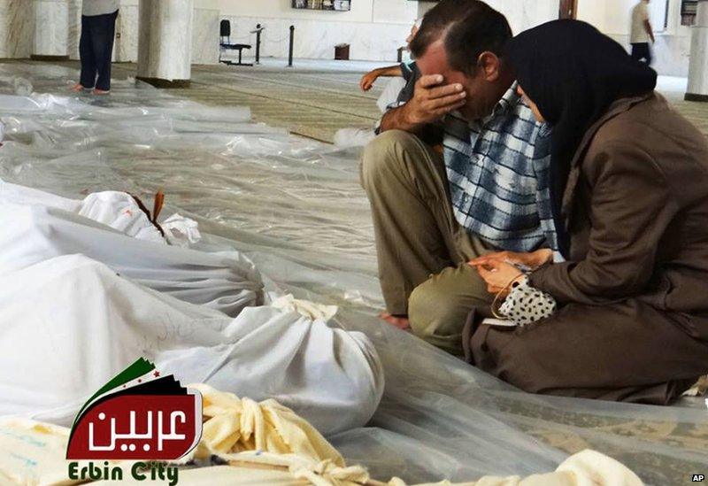 Image provided by Syrian opposition activists purportedly showing man and woman mourning next to bodies wrapped in shrouds in Irbin, Damascus (21 August 2013)