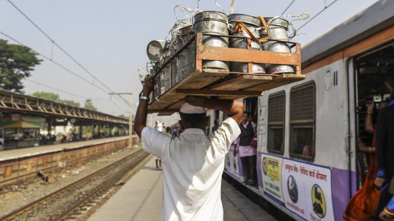 Dabbawala Dasharath Kedari carries a crate of tiffin boxes while walking past a train at the Santacruz railway station in Mumbai, India