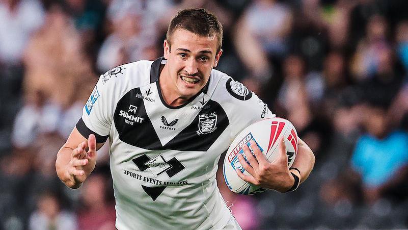Jake Arthur runs with the ball wearing a white and black Hull FC shirt