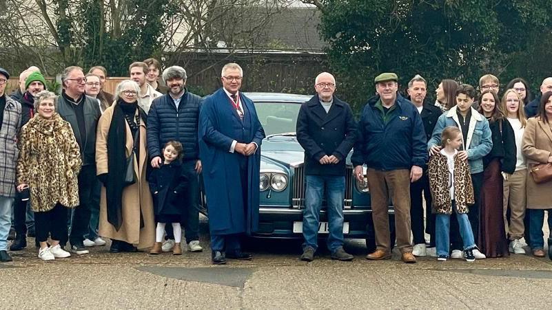 Mr Adams stands in front of his Rolls Royce surrounded by his family and the grown up children he had previously fostered, some of which have their own children with them.